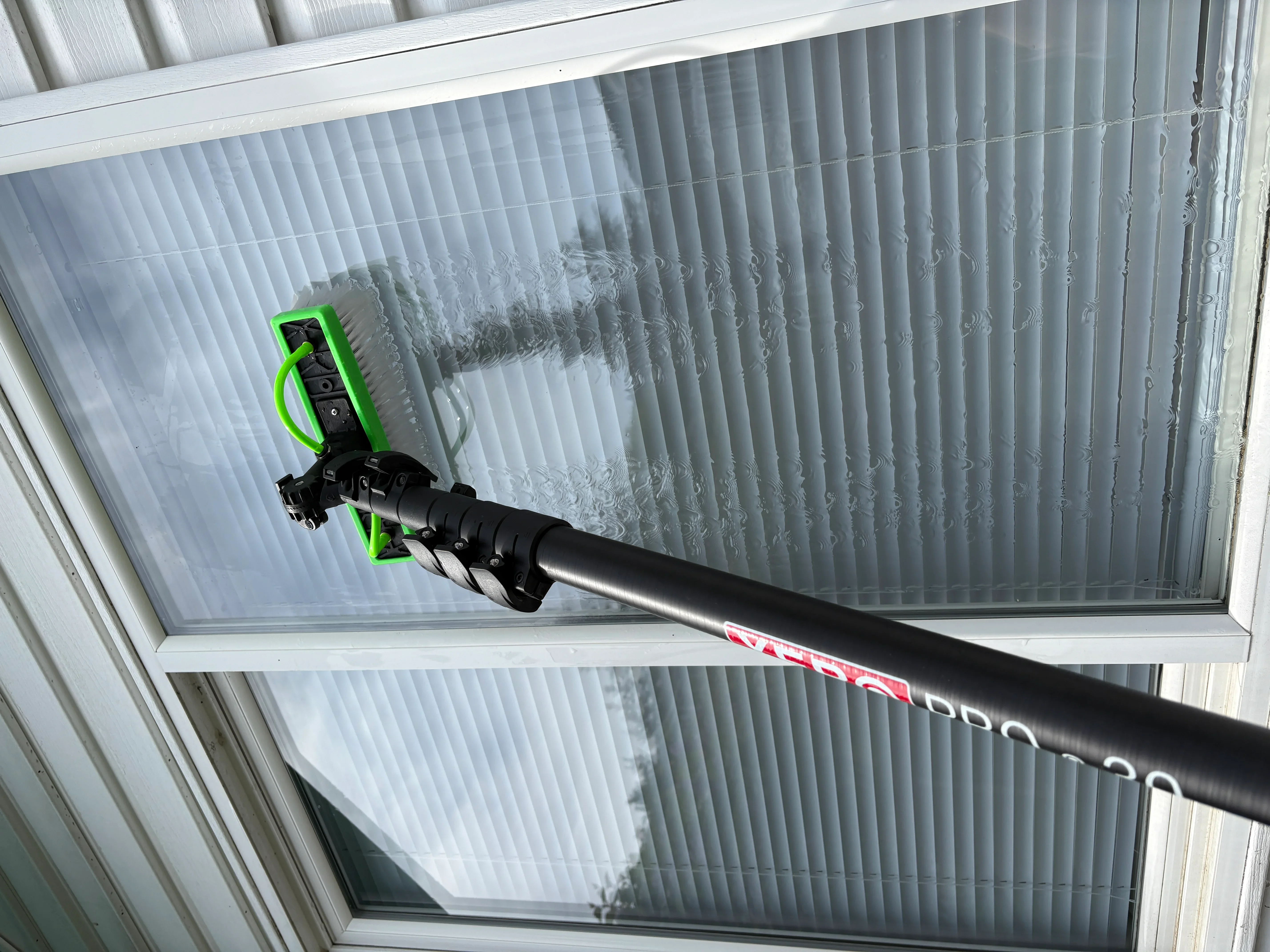 Pressure washing vertical blinds with green spray nozzle attachment, removing dust and dirt buildup