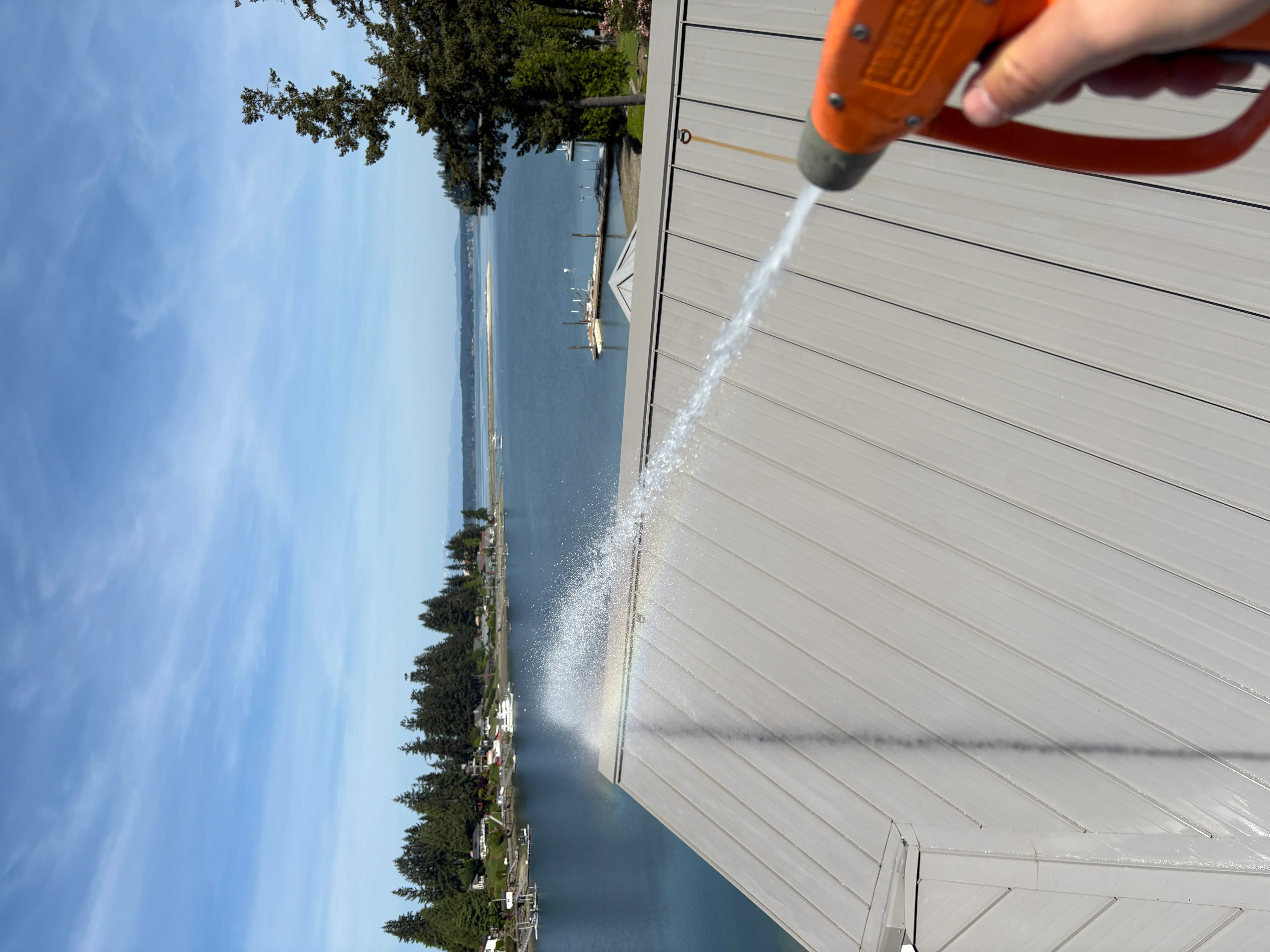 Pressure washing driveway with orange and gray equipment, horizontal siding visible