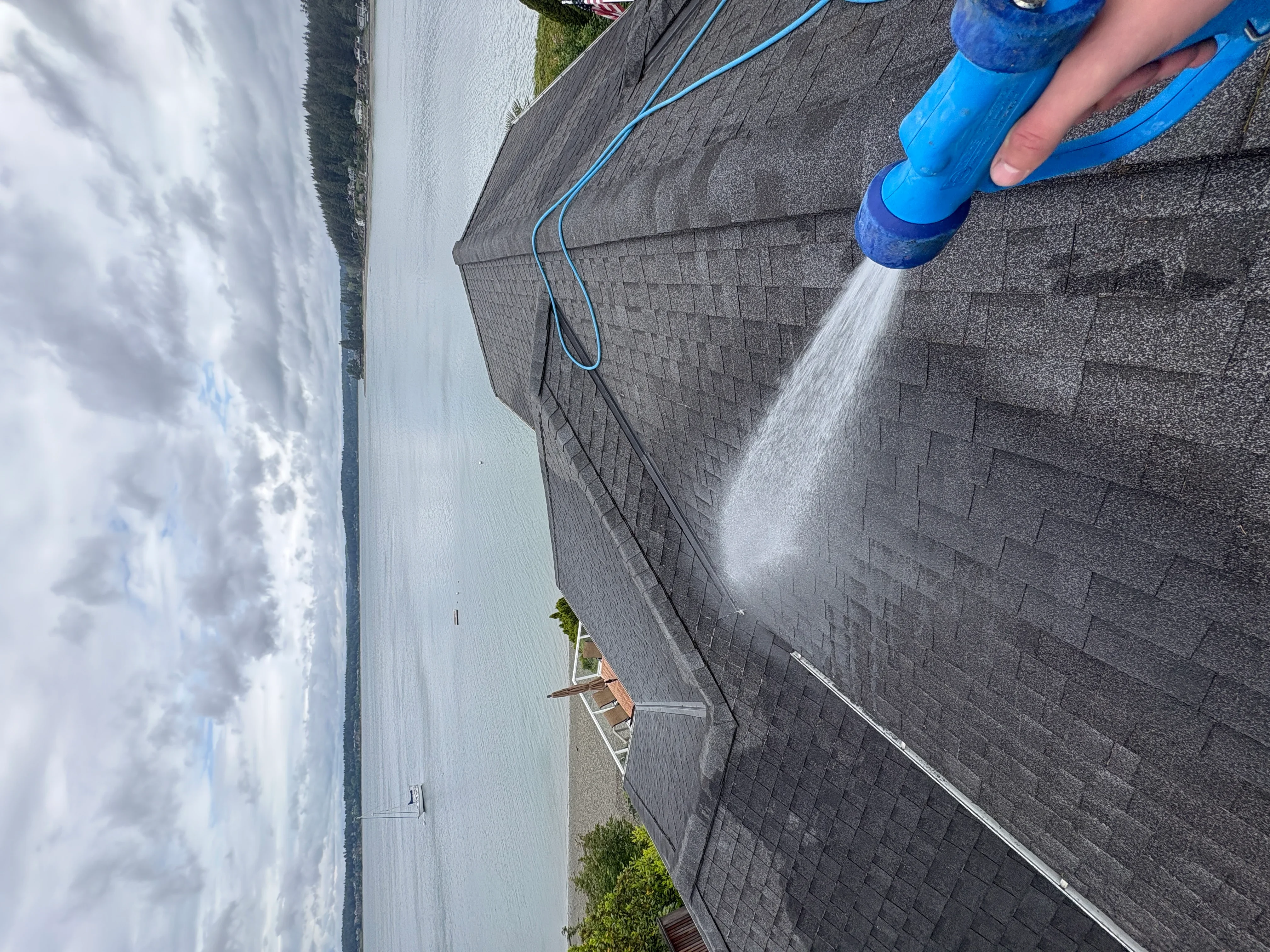 Pressure washing asphalt shingle roof with blue nozzle and hose
