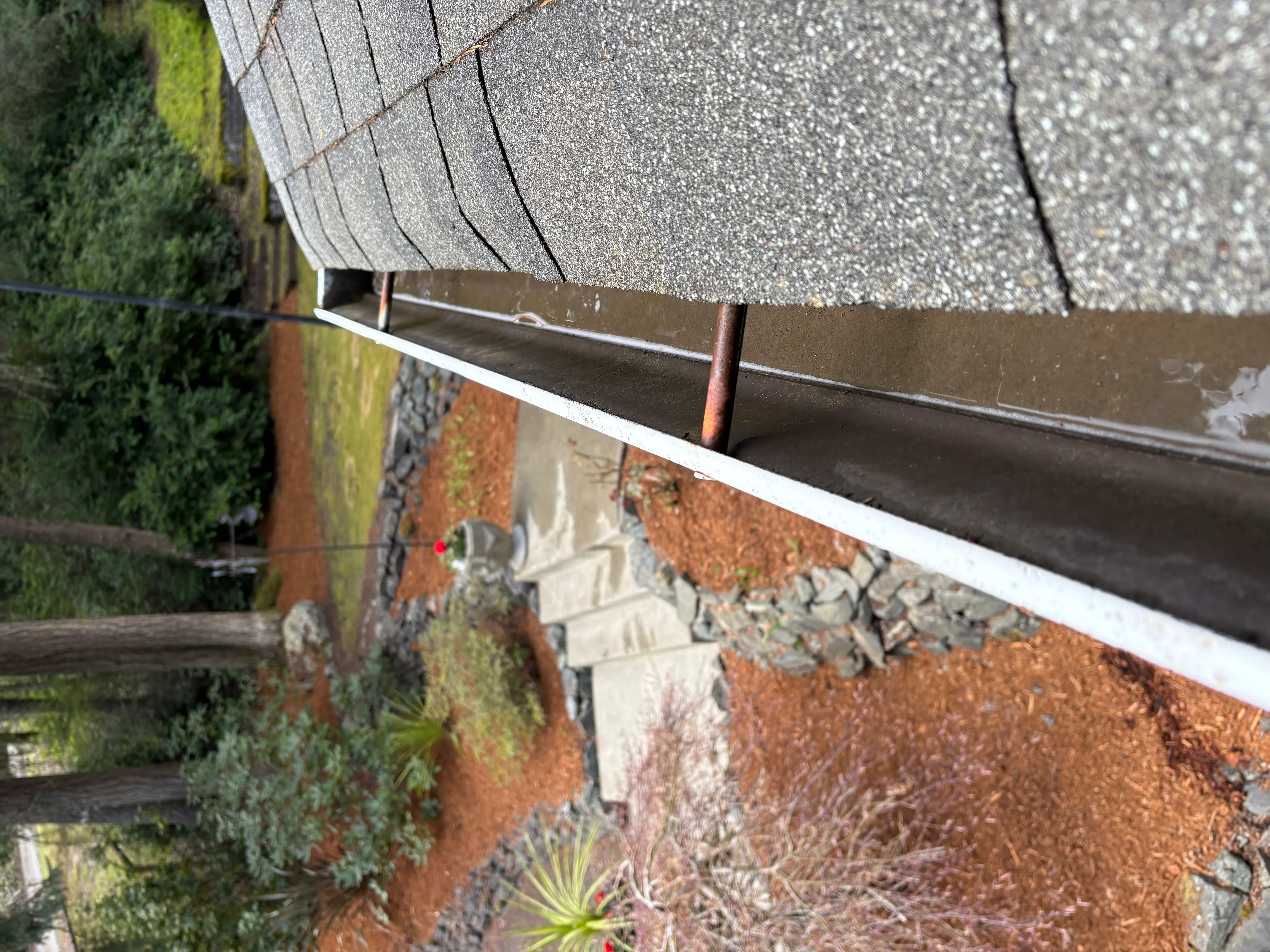 Clean aluminum gutter with downspout installed on brick home with asphalt shingle roof