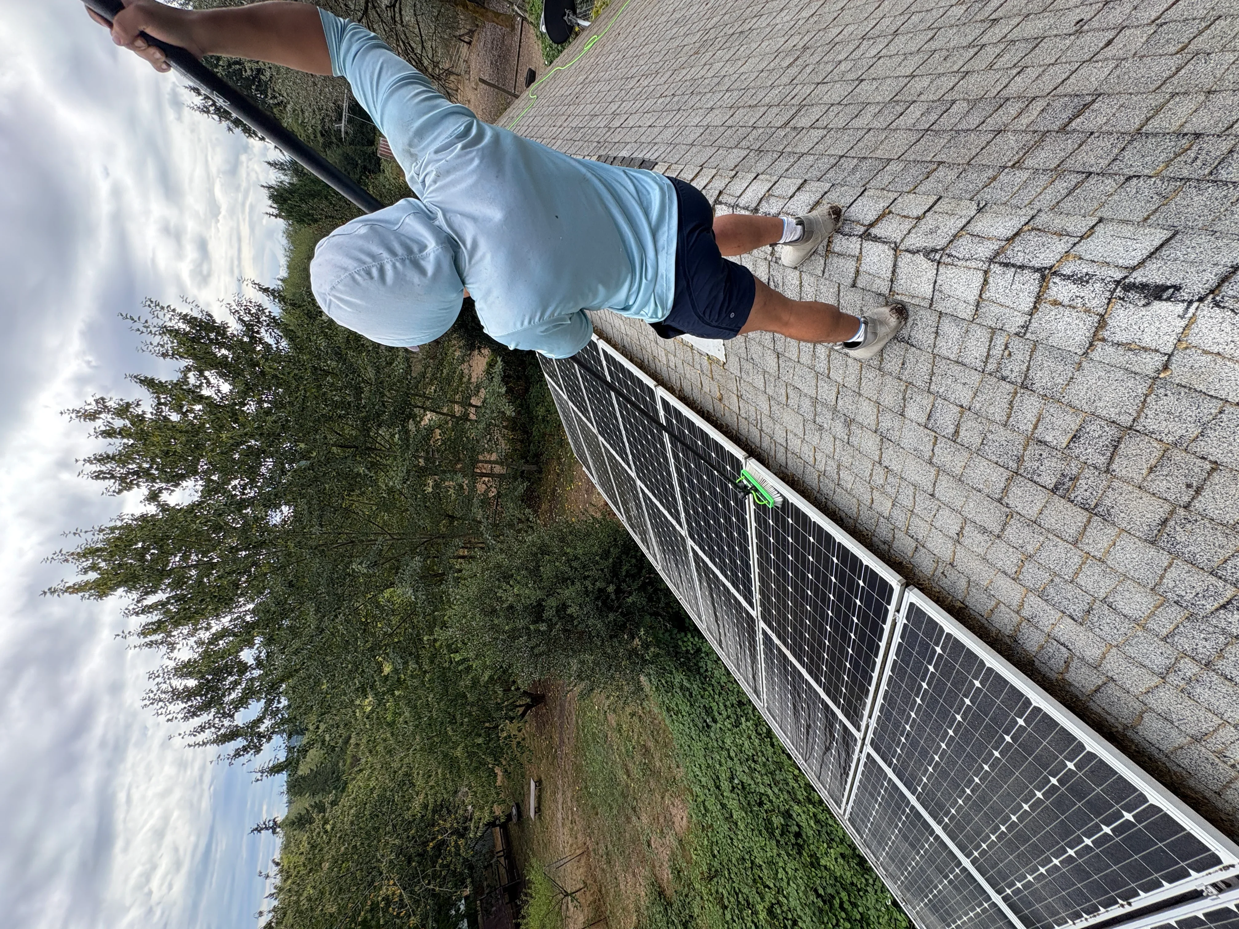 Technician cleaning solar panels on residential roof with white metal frame and mounting system