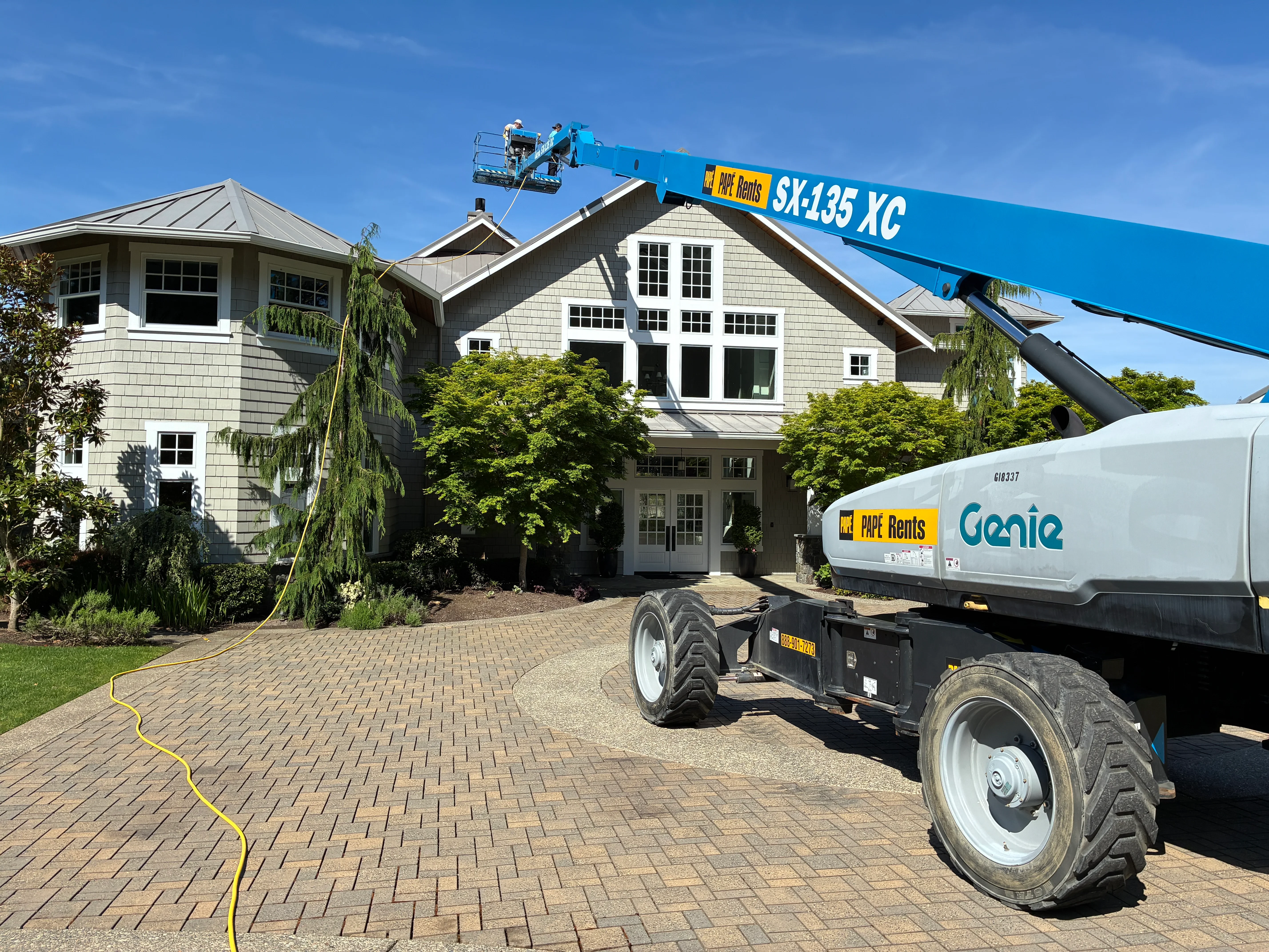 Pressure washing residential driveway and home exterior with shingle siding and metal roof