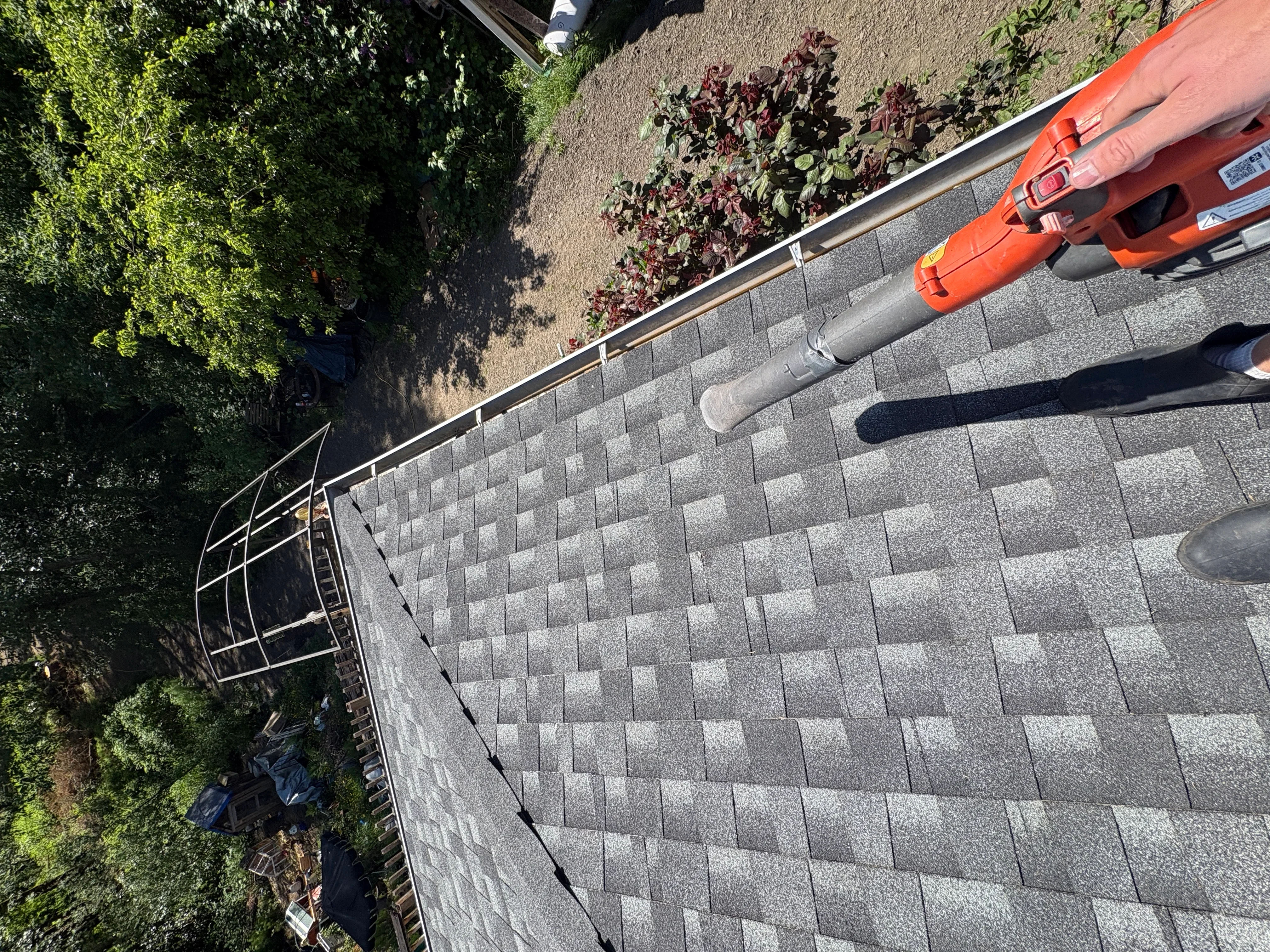 Technician cleaning asphalt shingle roof and gutters with pressure washing equipment