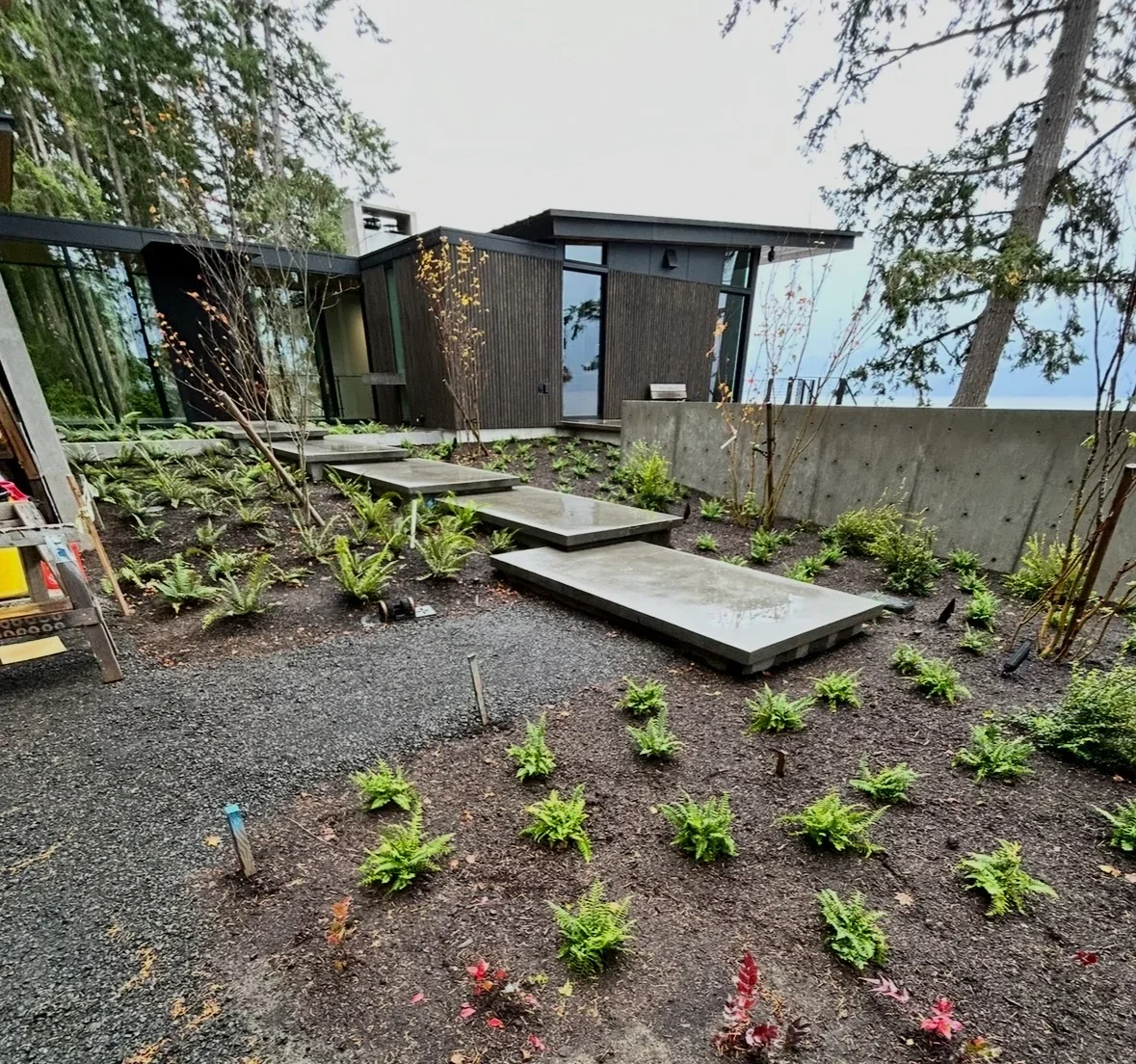 Pressure-washed concrete stepping stones and gravel pathway leading to modern dark metal home with retaining wall