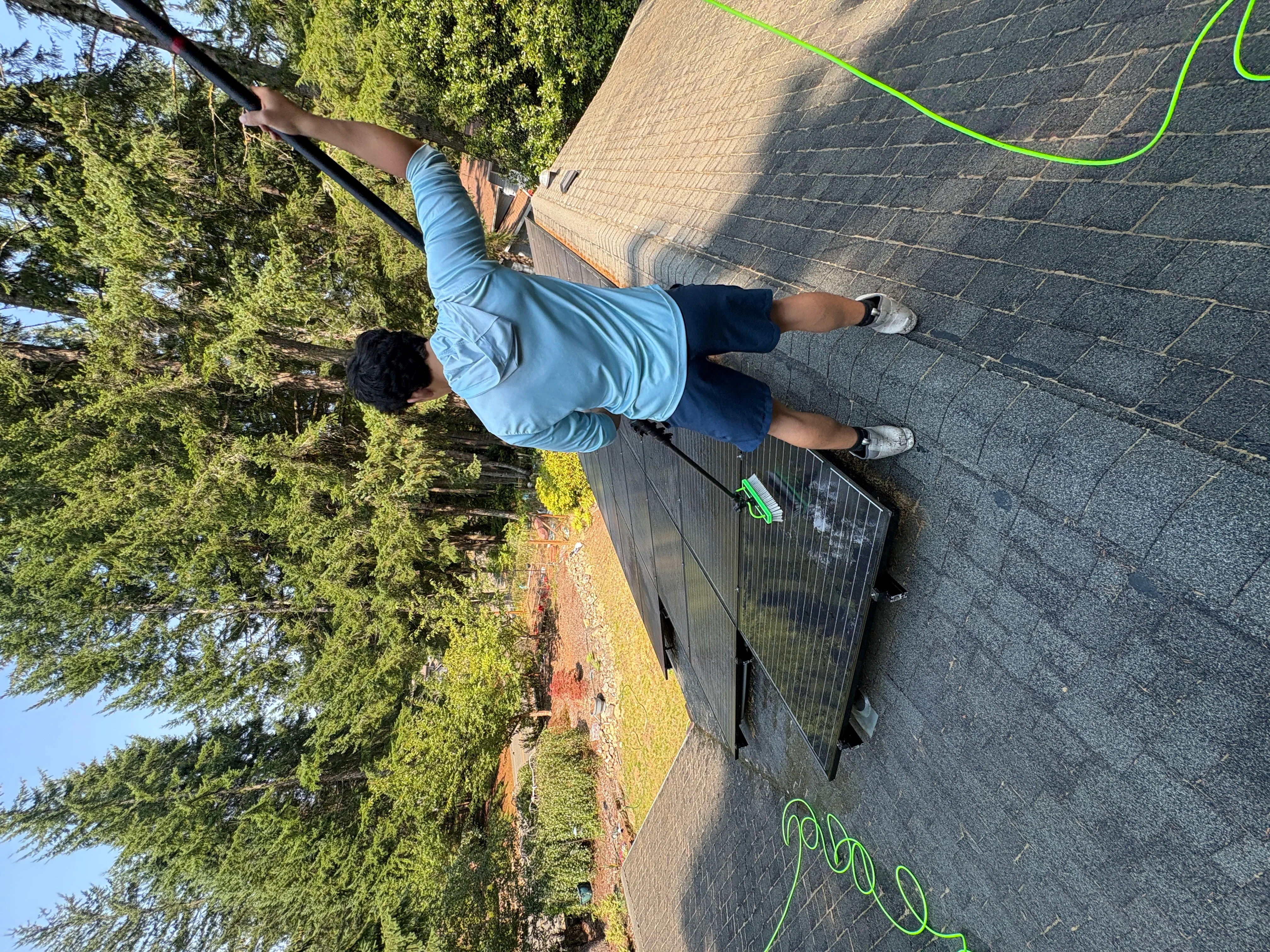Technician cleaning residential roof gutters and asphalt shingles with pressure washing equipment